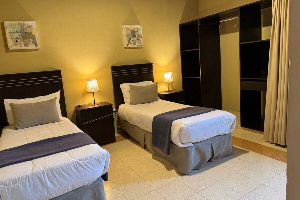 A hotel room with two beds, nightstands, bedside lamps, a wardrobe, and artwork on the walls.