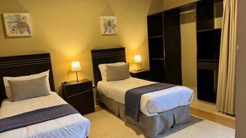 Habitación de hotel con dos camas, mesitas de noche, lámparas de lectura, un armario y obras de arte en las paredes.