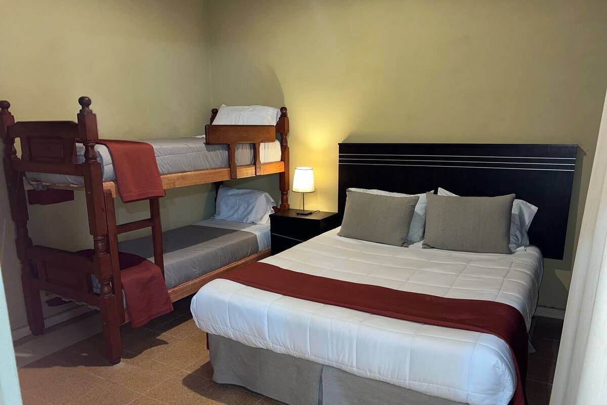 A room with a bunk bed, a single bed, and a nightstand with a lamp.