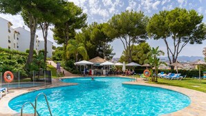 A swimming pool with a stone deck, surrounded by trees and a bar area. - Apartment 'Margarita In Miraflores' with Sea Views, Shared Pool and Wi-Fi (Las Lagunas de Mijas)