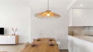 A modern kitchen with white cabinets, a wooden dining table with four chairs, and a hanging light fixture. - Apartment 'Margarita In Miraflores' with Sea Views, Shared Pool and Wi-Fi (Las Lagunas de Mijas)