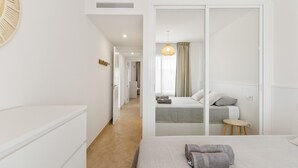 A hotel room with a bed, a small table, a chair, a wardrobe, and a hallway leading to another room. - Apartment 'Margarita In Miraflores' with Sea Views, Shared Pool and Wi-Fi (Las Lagunas de Mijas)