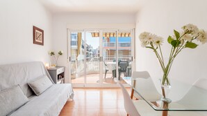 A modern living room with a sofa, a glass dining table, and chairs. There is a balcony with a view of buildings. - Apartment 'Gran Playa Dreams' with Sea View, Wi-Fi and Air Conditioning (Santa Pola)