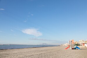 Una playa con cielo despejado, una montaña distante y edificios al fondo.