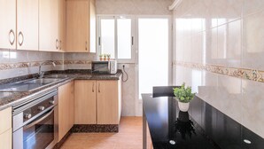 A kitchen with wooden cabinets, a microwave, a sink, and a potted plant on the counter. - Apartment 'Gran Playa Dreams' with Sea View, Wi-Fi and Air Conditioning (Santa Pola)
