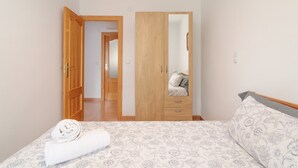 A bedroom with a bed, a wooden wardrobe, a mirror, and a door leading to another room. - Apartment 'Gran Playa Dreams' with Sea View, Wi-Fi and Air Conditioning (Santa Pola)