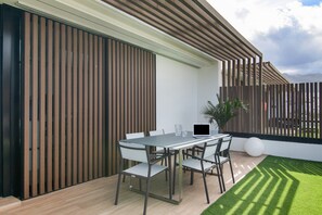 Un espacio moderno al aire libre con comedor, una mesa, sillas, una computadora portátil y una planta en maceta.
