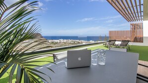Un ordinateur portable est posé sur une table, offrant une vue sur l’océan et une zone herbeuse.