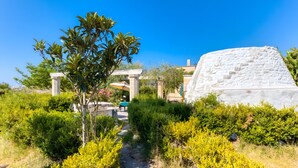 Un sendero en un jardín que conduce a un edificio con fachada blanca y una gran roca blanca.