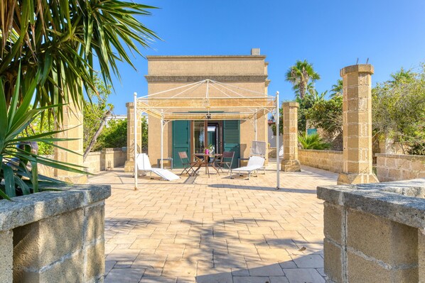 A courtyard with a covered seating area, a stone wall, and a building entrance.