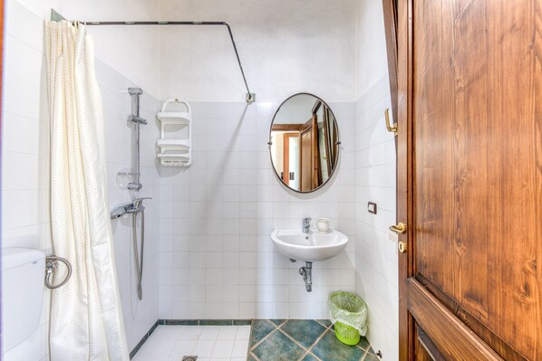 Un baño con ducha, lavamanos, espejo y puerta de madera.