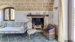 Una habitación con techo de ladrillo, chimenea, cama, silla de mimbre y ventana.