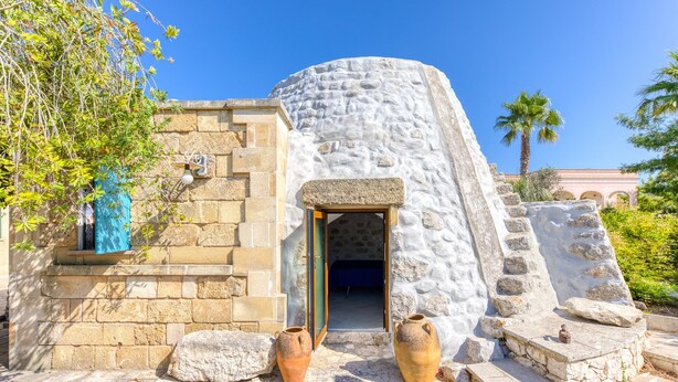 Un edificio de piedra con una entrada circular, dos jarrones grandes y una palmera al fondo.