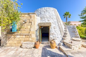 A stone building with a circular entrance, two large vases, and a palm tree in the background.