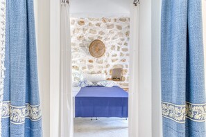 A room with a stone wall, a bed with a blue bedspread, and blue curtains with a pattern.