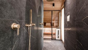A modern bathroom with dark marble walls, a wooden ceiling, and a glass shower enclosure.