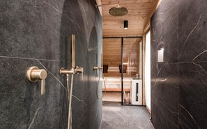 Un baño moderno con paredes de mármol oscuro, techo de madera y cabina de ducha de cristal.