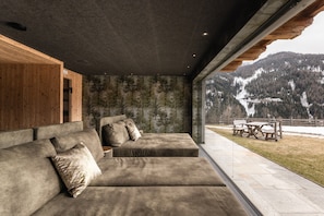 Un intérieur moderne avec un grand canapé d’angle, un mur d’accent en bois et une vue sur un paysage montagneux enneigé.