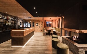 Un espace bar avec un comptoir en bois, des sièges avec des coussins et une cheminée.