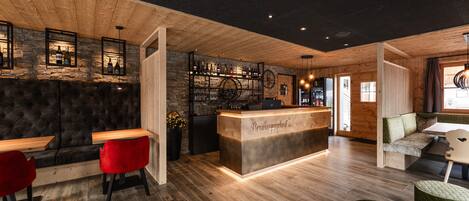 Eine Bar mit einer Holztresen, roten Stühlen und einer Steinwand.