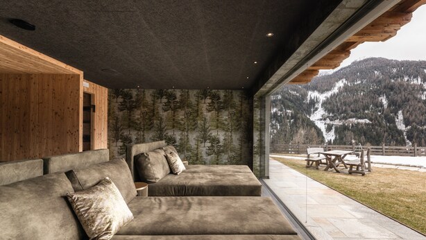 Un interior moderno con un sofá seccional grande, una pared de acento de madera y vistas a un paisaje montañoso nevado.