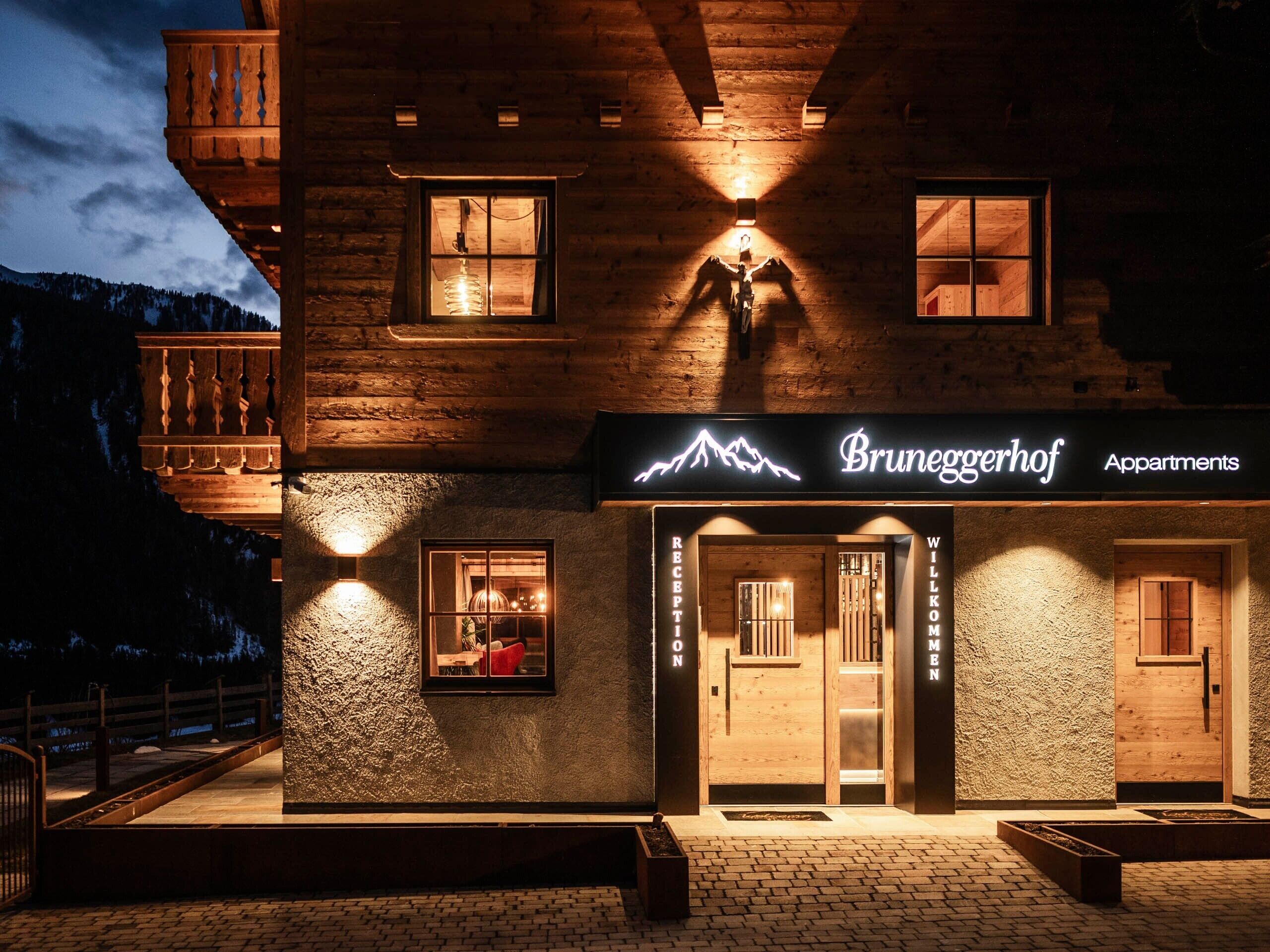 Un edificio de estilo cabaña de troncos con una zona de recepción, con el letrero 'Bruneggerhof Apartments', y el contorno de una montaña.
