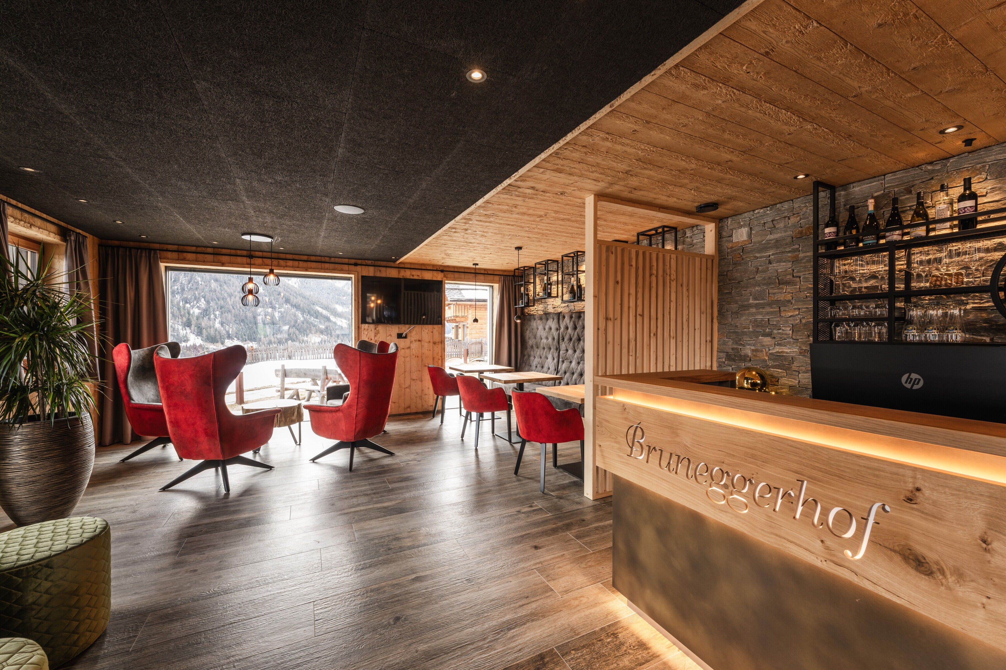 A restaurant with a wooden reception desk, red chairs, and a bar area with bottles and glasses.