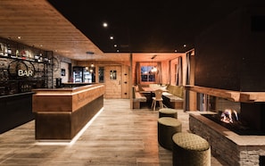 A bar area with a wooden counter, seating with cushions, and a fireplace.