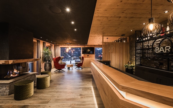 A modern bar area with wooden flooring, a reception desk, and a large window offering a view of the outdoors.