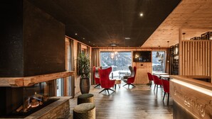 Un interior moderno con chimenea, sillas rojas, piso de madera y vistas a las montañas.