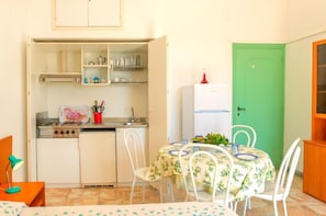 A compact kitchen with a dining area, a green door, and a small refrigerator.