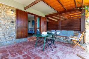 A patio area with a stone wall, wooden door, green metal table, and chairs. - Holiday Home 'Casa 2 Punta Negra' with Sea View, Private Terrace and Air Conditioning (Stintino)