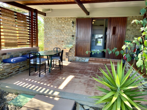 Une terrasse en pierre avec une table et des chaises, une porte en bois et une vue sur la cuisine.