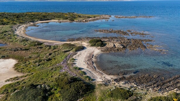 Vista aérea de un paisaje costero con aguas cristalinas, costas rocosas y montañas a lo lejos.