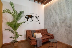 Une pièce avec un canapé en cuir marron, une table basse en verre, une grande plante en pot et une carte du monde accrochée au mur.