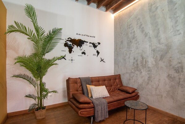 Ein Zimmer mit einem braunen Ledersofa, einem Glastisch, einer großen Topfpflanze und einer Weltkarte an der Wand.