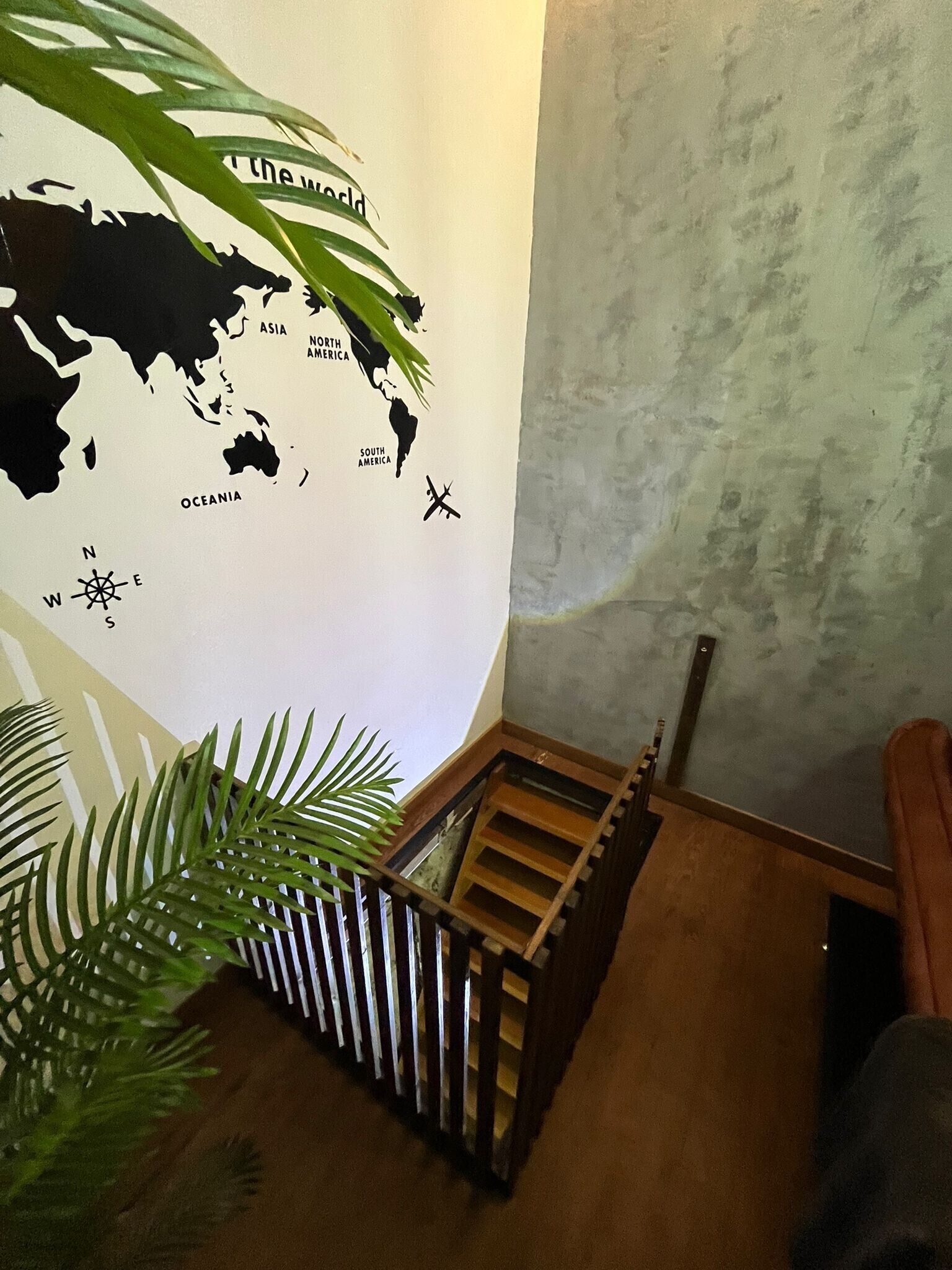 Una escalera con barandilla de madera, un mapa mundial en la pared y una planta en maceta.