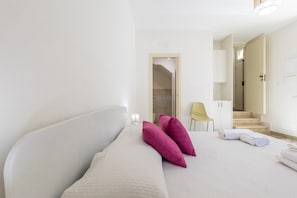 A hotel room with a bed, pillows, a chair, a desk, and a bathroom visible through an open door.