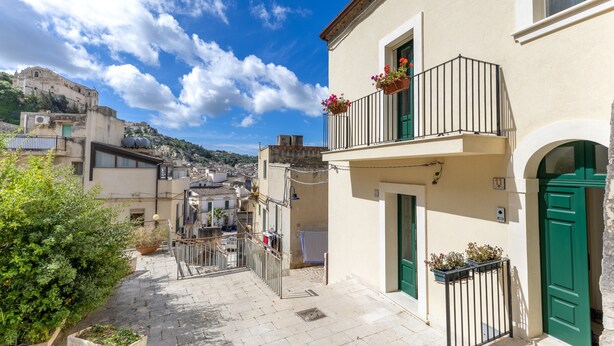 A narrow street with buildings, a balcony with flowers, and a green door. - Room 'Lì' with Mountain View, Wi-Fi and Air Conditioning (Scicli)