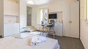 Quarto de hotel com cama, escrivaninha, televisão e cozinha compacta.