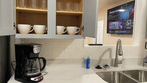Una cocina con cafetera, lavamanos y un televisor que muestra 'Stranger Things'.