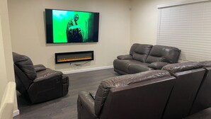 Una sala de estar moderna con un televisor de pantalla plana montado en la pared, sofás de cuero reclinables y una chimenea empotrada.