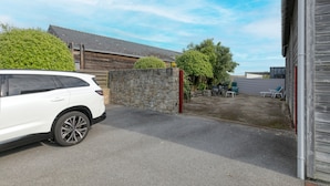 A white SUV parked in a driveway with a stone wall, a wooden building, and a clear sky.