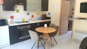 A compact kitchen with a dining area, including a table with chairs, a microwave, a kettle, and a toaster.