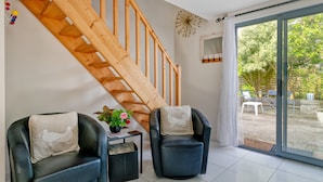 A modern room with a wooden staircase, two leather armchairs, a small table with a vase of flowers, and a sliding glass door leading to an outdoor area.
