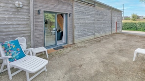 A building with a sliding door, a small outdoor seating area with white chairs, and a clear sky.