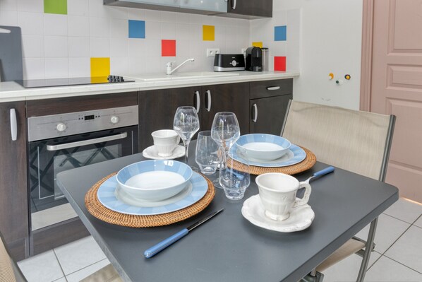 Una cocina moderna con una mesa para dos, con platos azules y blancos, vasos transparentes y un cuchillo.
