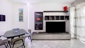 Ein modernes Wohnzimmer mit Esstisch, Stühlen, einem Flachbildfernseher und eingebauten Regalen.