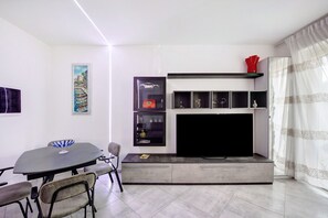 A modern living room with a dining table, chairs, a flat-screen TV, and built-in shelves.