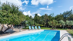 A swimming pool with blue tiles, surrounded by trees and a building with a sloped roof.
